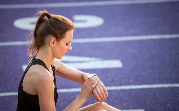 运动妇女坐在跑道上看健身智能手表 — 图库照片