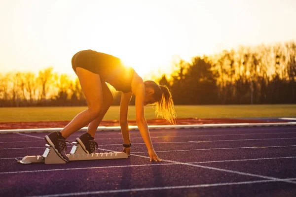 Young athletic woman on running track starting from start line