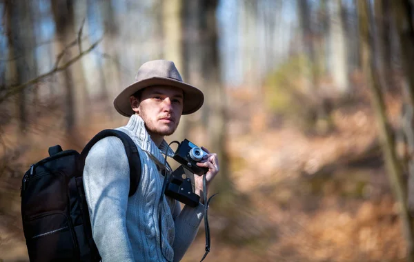 Traveler man with vintage camera and backpack walking in autumn forest