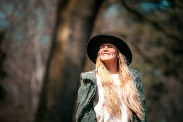 Portrait of young smiling woman in hat walking in autumn forest