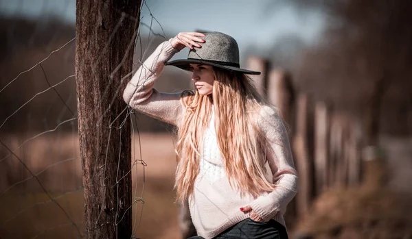 洒落たお帽子を農村のフェンスに近いポーズの若い女性 — ストック写真