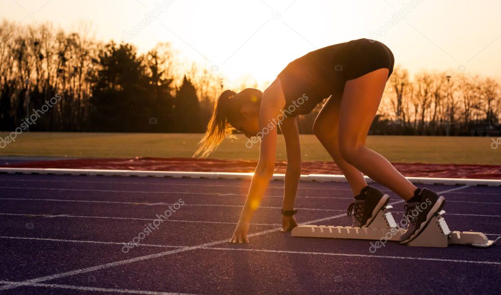 Young athletic woman on running track starting from start line