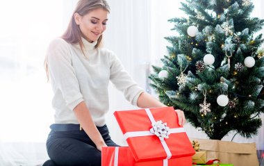 Noel ağacının önündeki genç kadın Noel hediyelerini açıyor.