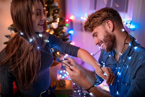 愉快的夫妇有乐趣与圣诞灯旁边的圣诞树在假日晚上 — 图库照片