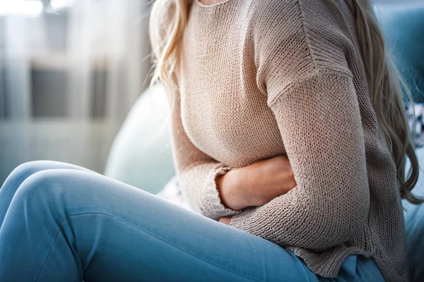 Evdeki kanepede otururken karın ağrısı çeken genç bir kadın.