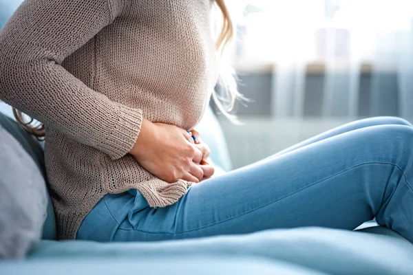 Evdeki kanepede otururken karın ağrısı çeken genç bir kadın.