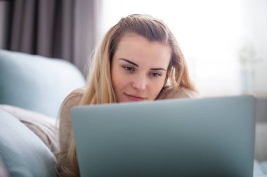 Gülümseyen kadın evde kanepede rahatlatıcı ve dinlenme yalan sırasında dizüstü bilgisayar ekranına bakarak
