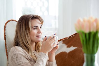 Mutlu kadın koltukta rahatlatıcı evde bardak sıcak çay veya kahve, olumlu duygular ile oturuyordu
