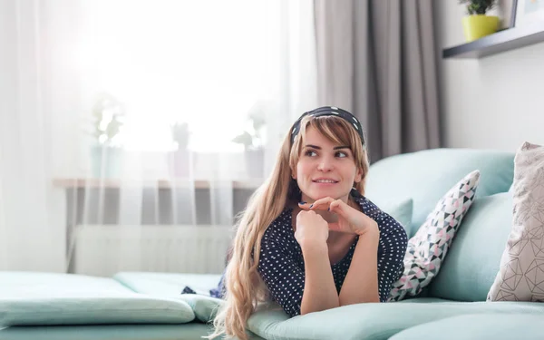 Happy woman lying on couch and thinking about something at home, casual style indoor shoot