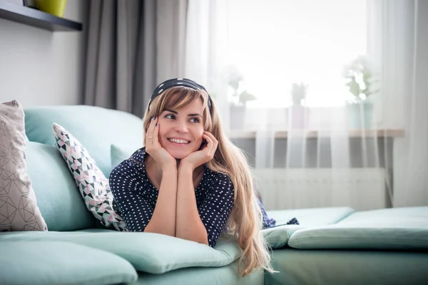 Happy woman lying on couch and thinking about something at home, casual style indoor shoot