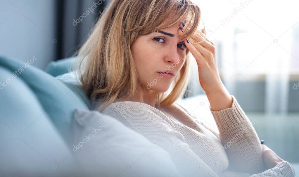 Sad woman sitting on sofa at home looking at camera, thinking about important things