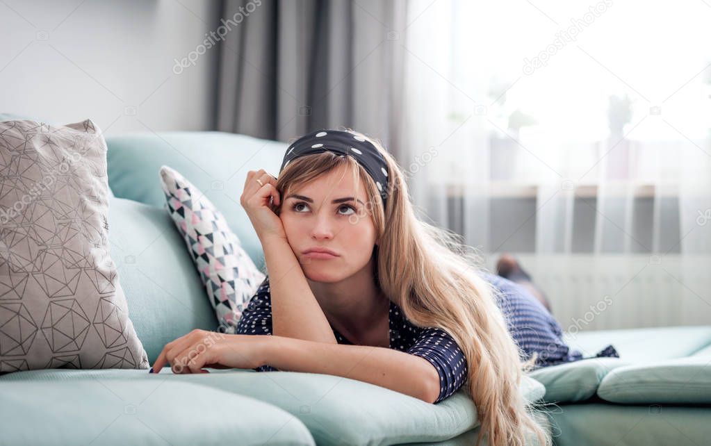 Sad disappointed woman lying on couch and thinking about something at home, casual style indoor shoot