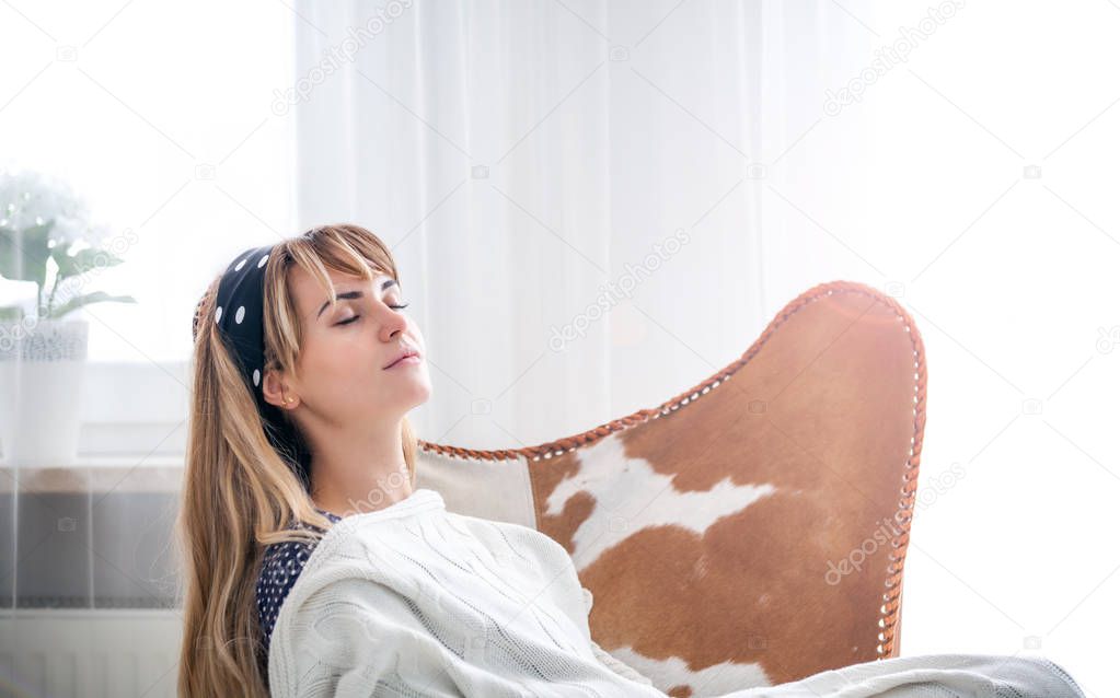 Leisure time at home, young woman sleeping with blanket relaxing on armchair in bright living room