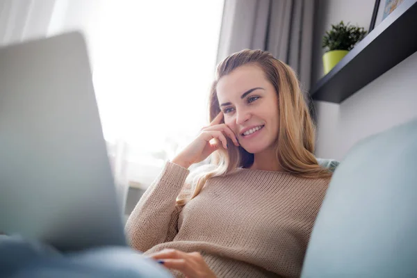 Happy woman at home using laptop sitting on sofa, online working at home