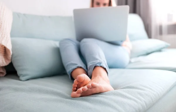 Happy woman at home using laptop sitting on sofa, online working at home