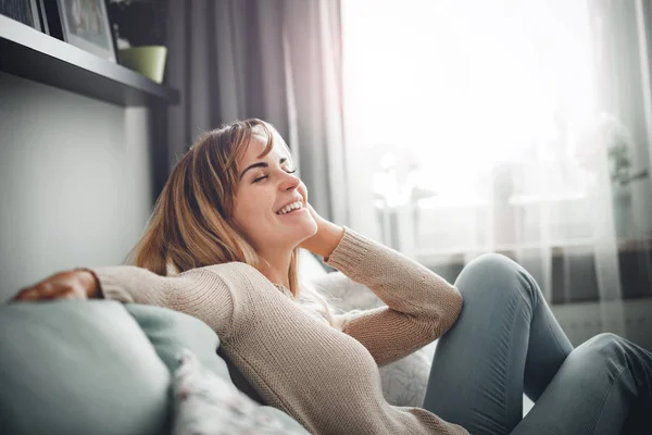 Cheerful smiling woman full of positive emotions sitting on sofa at home