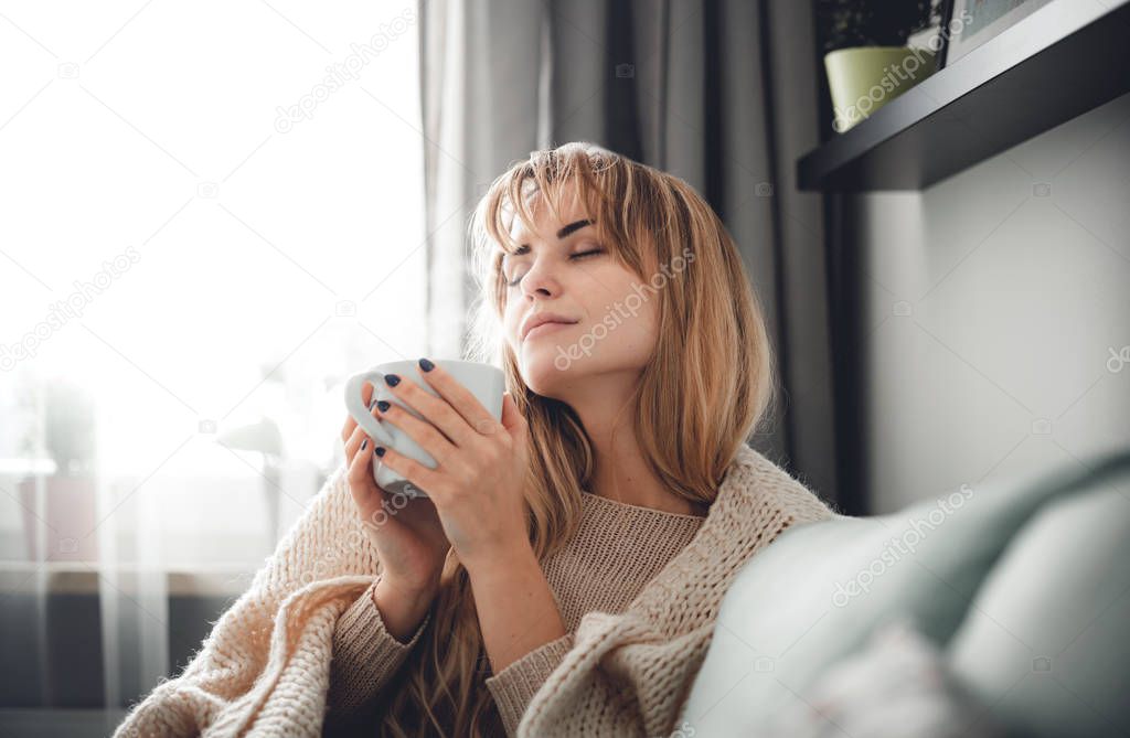 Happy woman in soft sweater relaxing at home with cup of hot tea or coffee