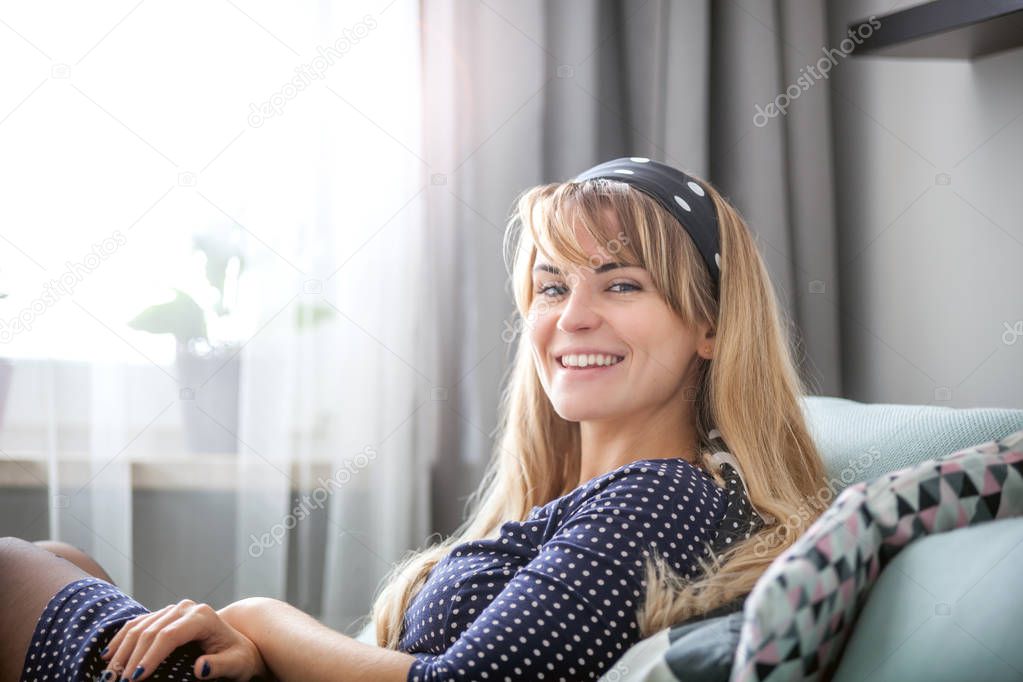 Cheerful young woman smiling and looking at camera sitting on sofa at home