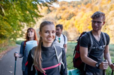 Sırt çantası ile gülümseyen genç yürüyüşçü kadın arkadaşlarının eşliğinde trekking