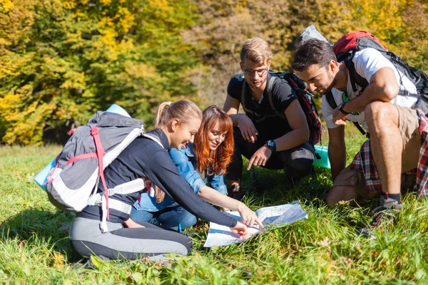 Group of hikers with backpacks looking at map and planning further trekking trail