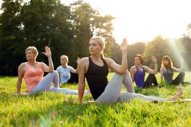 Gün batımı sırasında parkta yoga yapan insanların karışık yaş grubu
