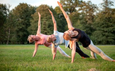 Parkta yoga, gün batımında poz veren bir grup karışık yaş kadını.