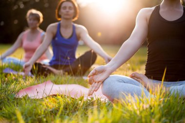 Parkta yoga yapan ve gün batımında meditasyon yapan bir grup karışık yaş kadını.