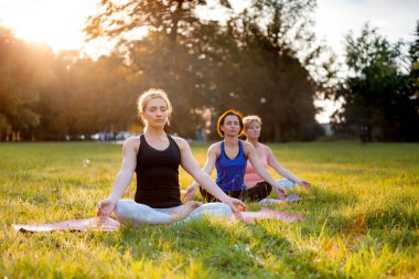 Parkta yoga yapan ve gün batımında meditasyon yapan bir grup karışık yaş kadını.