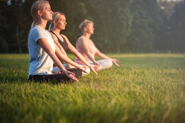 Parkta yoga yapan ve gün batımında meditasyon yapan bir grup karışık yaş kadını.