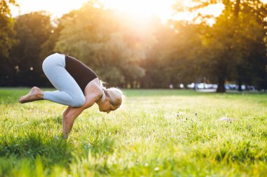 Yoga parkta, orta yaş kadının bakasana egzersiz vinç poz yapması