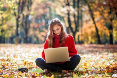 Laptop ve kamera açık otururken çimenlikte kullanan güzel kadın