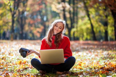 Laptop ve kamera açık otururken çimenlikte kullanan güzel kadın