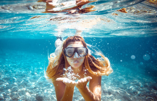 Snorkeling woman blowing a kiss underwater in the tropical sea