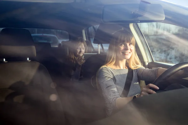 Maman conduisant une voiture alors que sa fille est assise sur le siège arrière et utilise une tablette numérique Images De Stock Libres De Droits