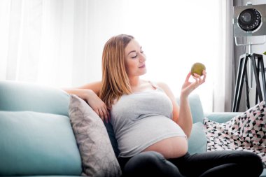 Hamilelik sırasında beslenme ve diyet, evde kanepede oturan meyve yiyen hamile kadın