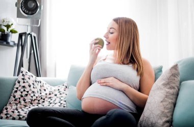 Hamilelik sırasında beslenme ve diyet, evde kanepede oturan meyve yiyen hamile kadın