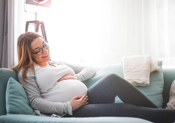 Fiatal terhes nő ül a kanapén a nappaliban — Stock Fotó