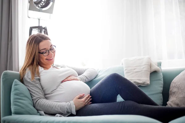 Fiatal terhes nő ül a kanapén a nappaliban — Stock Fotó