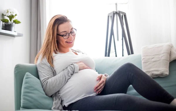 Fiatal terhes nő ül a kanapén a nappaliban — Stock Fotó