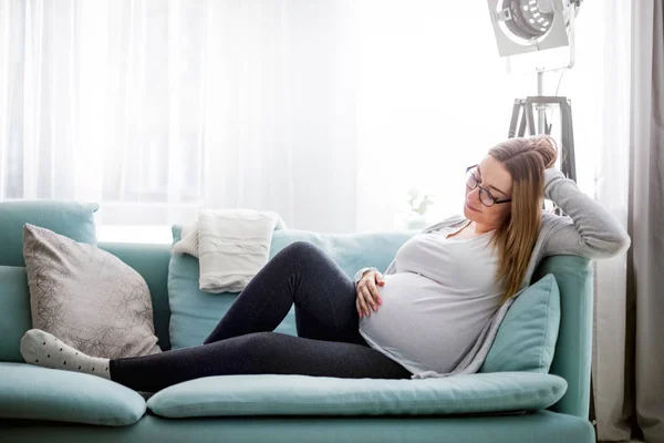 Mladá těhotná žena sedí na gauči v obývacím pokoji — Stock fotografie