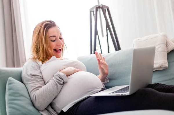 Těhotná žena videokonverzace s rodinou na přenosném počítači mávající ruku na obrazovku — Stock fotografie