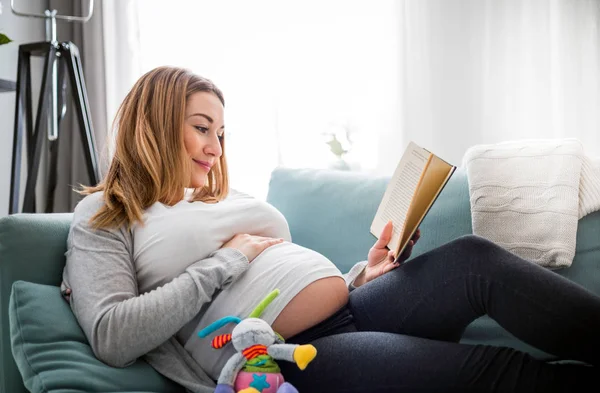 Беременная Женщина Отдыхает Диване Читая Книгу Глядя Живот — стоковое фото