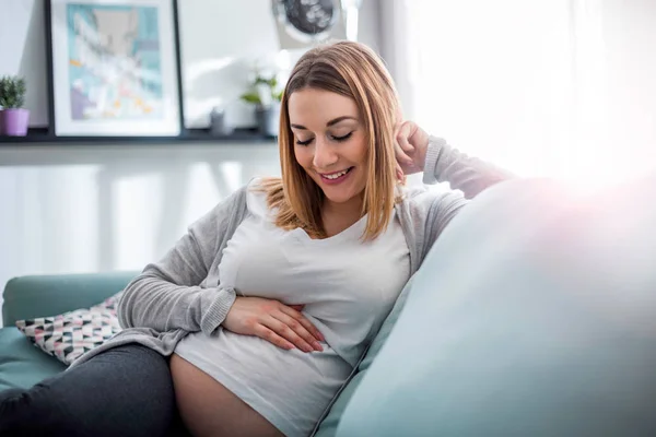 Schwangere entspannt auf Sofa zu Hause im sonnigen Wohnzimmer — Stockfoto