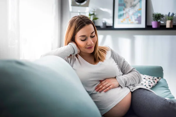 Schwangere entspannt auf Sofa zu Hause im sonnigen Wohnzimmer — Stockfoto