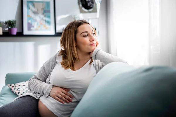 Terhes nő pihentető kanapén otthon napfényes nappaliban — Stock Fotó