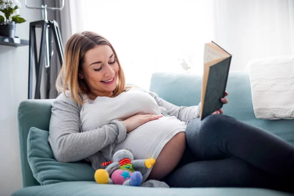 Беременная Женщина Отдыхает Диване Читая Книгу Глядя Живот — стоковое фото