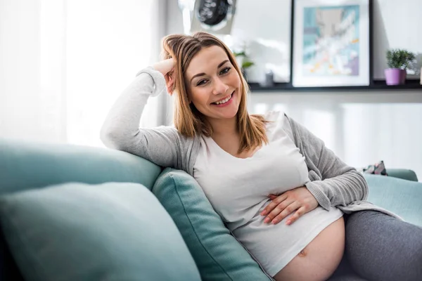 Femme enceinte se détendre sur le canapé à la maison et regarder la caméra — Photo