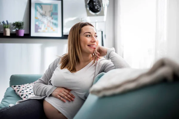 Mulher grávida relaxando no sofá em casa na sala de estar ensolarada — Fotografia de Stock