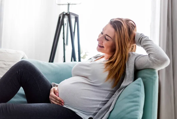 Беременная женщина отдыхает дома на диване — стоковое фото