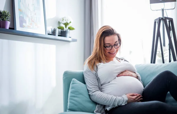Беременная женщина отдыхает дома на диване — стоковое фото